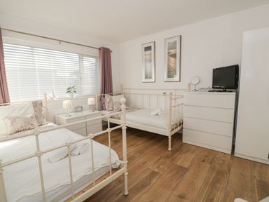 A bedroom with two single beds a white dresser a wardrobe and a window with blinds and curtains at The Gables in Tywyn