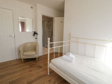 A bedroom with a single bed with rolled towels a beige armchair and an open door leading to a bathroom at The Gables in Tywyn