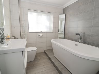 A bathroom with a bathtub on a raised platform a toilet and a sink under a window with blinds at The Gables in Tywyn