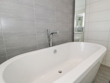A white freestanding bathtub with chrome fixtures against grey tiled walls in a bathroom at The Gables in Tywyn