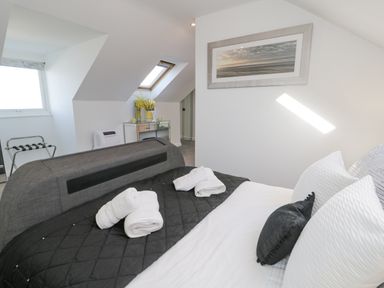 A bedroom with a black and white bedspread and rolled towels on the bed near a mirrored dresser with yellow flowers at The Gables in Tywyn