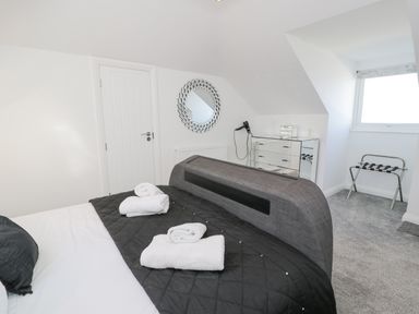 A bedroom with a bed with white towels on black quilt a mirrored chest of drawers a round decorative mirror and a window at The Gables in Tywyn