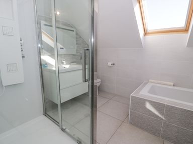 A bathroom with a shower enclosure a bathtub a sink with a cabinet a toilet and a skylight window at The Gables in Tywyn