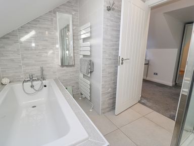 A bathroom with a bathtub a towel rail and a partially open door leading to a carpeted room at The Gables in Tywyn