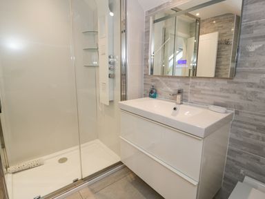 A bathroom with a walk in shower and a white sink cabinet with mirror above at The Gables in Tywyn