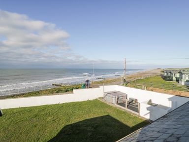 A coastal view with grassy yard and white wall near the sea at The Gables in Tywyn