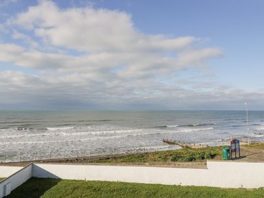 A coastal view with a grassy area and a white wall overlooking the sea and a cloudy sky at The Gables in Tywyn