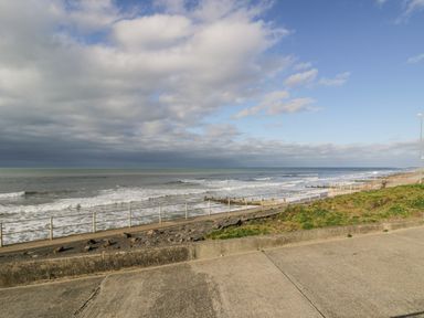 A concrete walkway next to a beach with waves and a cloudy sky at The Gables in Tywyn