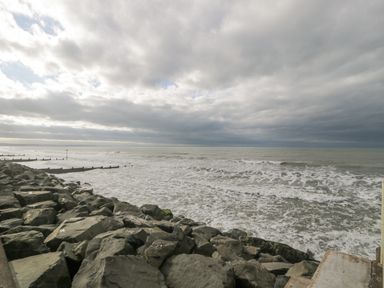 A rocky shoreline with waves coming in and a cloudy sky at The Gables in Tywyn