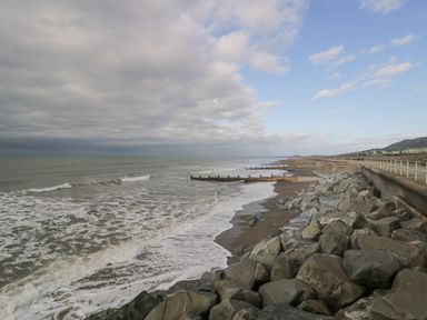 A rocky shoreline with a concrete seawall and groynes along the beach at The Gables in Tywyn