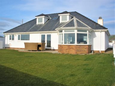A white house with a gray roof and a patio table with chairs on a lawn at The Gables in Tywyn