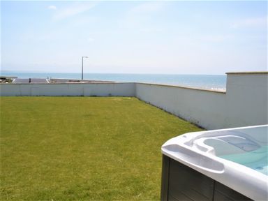A grassy outdoor area with a hot tub and a white wall overlooking the ocean at The Gables in Tywyn