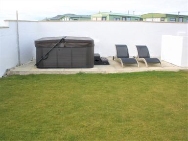 An outdoor area with a closed hot tub and two lounge chairs on a paved patio with grass in the foreground at The Gables in Tywyn