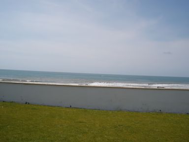 A grassy area with a white wall overlooking the ocean and a partly cloudy sky at The Gables in Tywyn