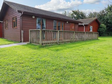A wooden house with a fenced patio and green grass surrounding it at Gwanda Tregolds near St Merryn