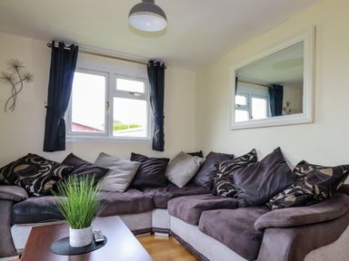 A living room with a sectional sofa and a table with a plant at Gwanda Tregolds near St Merryn