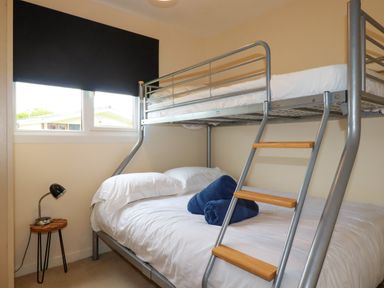 A bedroom with a metal bunk bed two blue towels on the lower bed a small wooden side table and a lamp at Gwanda Tregolds near St Merryn