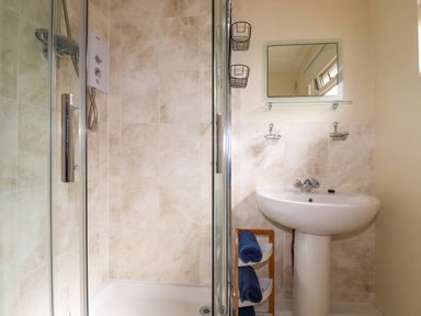 A bathroom with a shower enclosure, a pedestal sink, a mirror, and towel storage at Gwanda in Tregolds near St Merryn