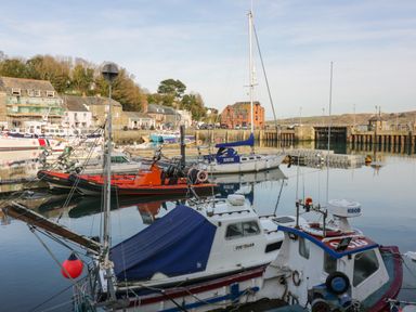 A harbor with several boats docked near buildings and a pier at Gwanda Tregolds near St Merryn
