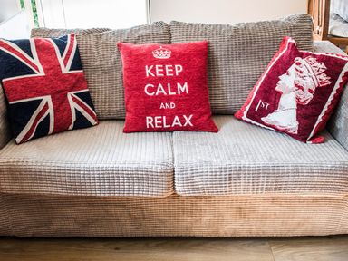 A beige sofa with three red themed cushions including a Union Jack flag cushion a Keep Calm And Relax cushion and a cushion with a profile of a queen at October House Holiday Cabin in Damerham