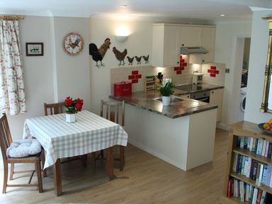 A kitchen with a dining table and chairs a countertop with a sink and stove and wall decorations at October House Holiday Cabin in Damerham