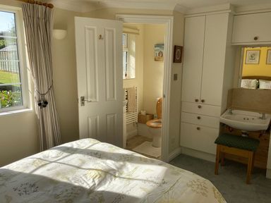 A bedroom with a bed near a window and an open door leading to a bathroom with a toilet and towel rail at October House Holiday Cabin in Damerham