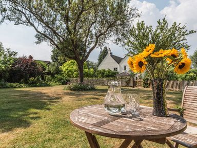 A garden with a wooden table holding a vase of sunflowers a glass jug and a drinking glass at October House Holiday Cabin in Damerham