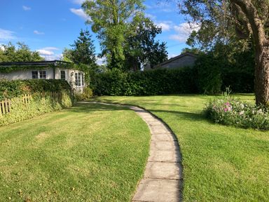 A garden with a curved stone path leading to a small building surrounded by hedges and trees at October House Holiday Cabin in Damerham