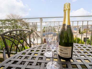 A balcony with a table holding a bottle of champagne and two empty champagne glasses at Fal View in Falmouth