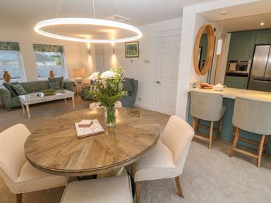 A dining area with a round wooden table and chairs next to a kitchen with bar stools and a living room with sofas at Fal View in Falmouth