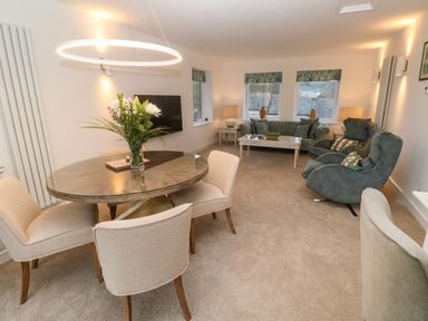 A living room with a round dining table with flowers on it and seating area with sofas and armchairs at Fal View in Falmouth