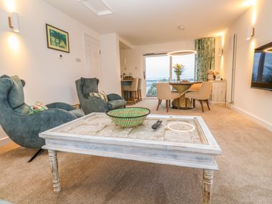 A living room with blue armchairs a white coffee table a round dining table with chairs and a wall mounted TV at Fal View in Falmouth