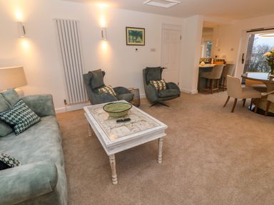 A living room with two armchairs, a sofa, a coffee table, and a dining area at Fal View in Falmouth