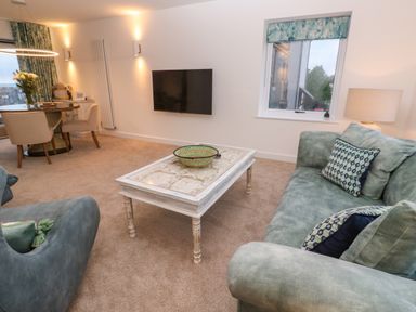A living room with green sofas white coffee table and wall mounted tv at Fal View in Falmouth