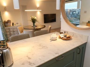 A kitchen counter with a teapot and basket of food and a round mirror reflecting buildings outside at Fal View in Falmouth