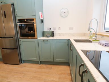A kitchen with green cabinets a stainless steel fridge an oven a sink with a curved faucet and a clock on the wall at Fal View in Falmouth