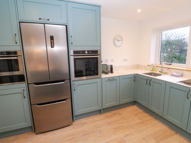 A kitchen with teal cabinets stainless steel refrigerator built in ovens wooden floor and a window above the sink at Fal View in Falmouth