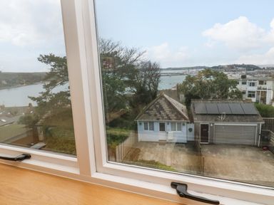 A view through a window showing a small house and a garage with solar panels near a body of water at Fal View in Falmouth