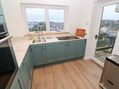 A kitchen with green cabinetry a sink an electric stove and a door leading to a balcony at Fal View in Falmouth