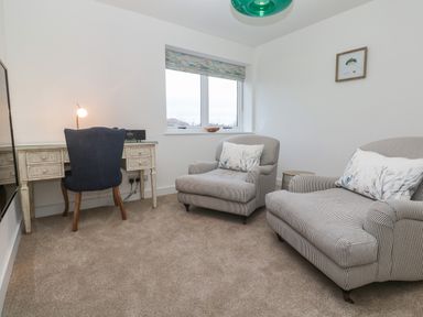 A small room with a desk and chair by the wall and two armchairs with cushions near a window at Fal View in Falmouth