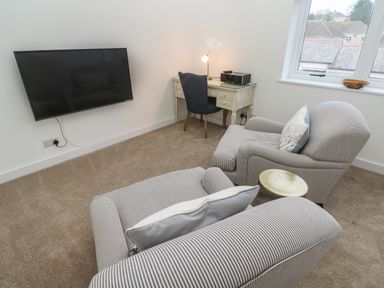 A room with two striped armchairs facing a wall mounted television and a desk with a chair and lamp at Fal View in Falmouth