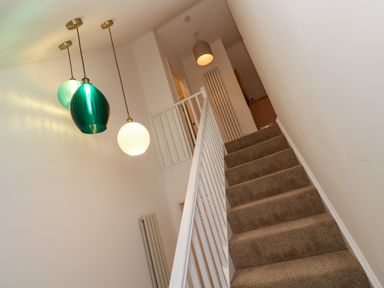 A carpeted staircase with white railing and pendant lights above at Fal View in Falmouth