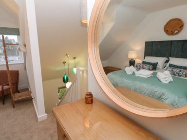A bedroom with a green bedspread reflected in a round mirror above a wooden dresser at Fal View in Falmouth