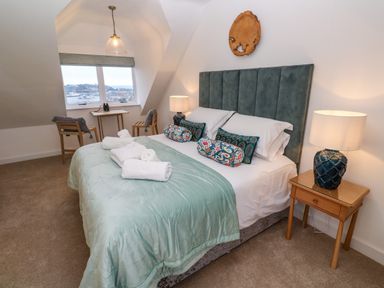 A bedroom with a double bed with colorful pillows bedside tables with lamps and two chairs by a window with a view at Fal View in Falmouth