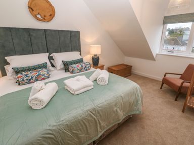 A bedroom with a double bed, towels on the bed, a nightstand with a lamp, a wooden chest, a chair, and a window at Fal View in Falmouth