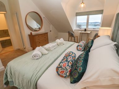 A bedroom with a bed and pillows next to a window with chairs and a table and a dresser with a round mirror at Fal View in Falmouth