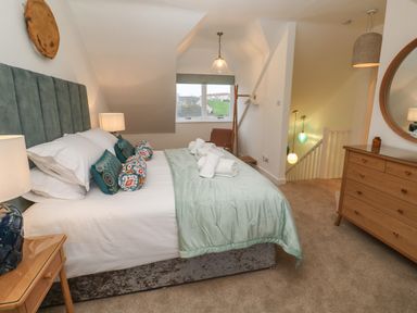 A bedroom with a bed and decorative pillows a wooden dresser a mirror a lamp and a window at Fal View in Falmouth