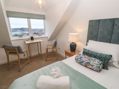 A bedroom with a bed bedside table lamp two wooden chairs small table and a window showing a harbor view at Fal View in Falmouth