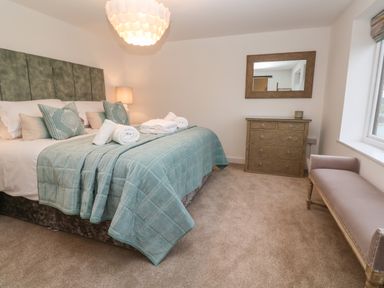 A bedroom with a double bed with pillows and towels a dresser with a mirror and a bench at Fal View in Falmouth