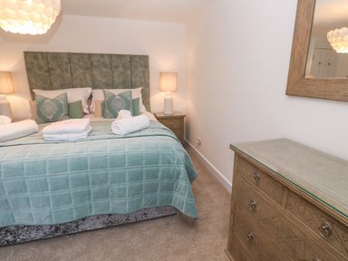A bedroom with a bed with pillows and towels and two bedside tables with lamps and a dresser with a mirror at Fal View in Falmouth